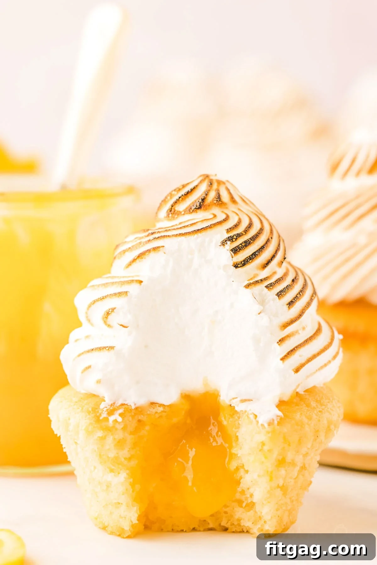Tangy Meringue Cloud Cupcakes 2 A delicious lemon meringue cupcake with a bite taken out, revealing the vibrant lemon curd filling and the fluffy white texture of the meringue.