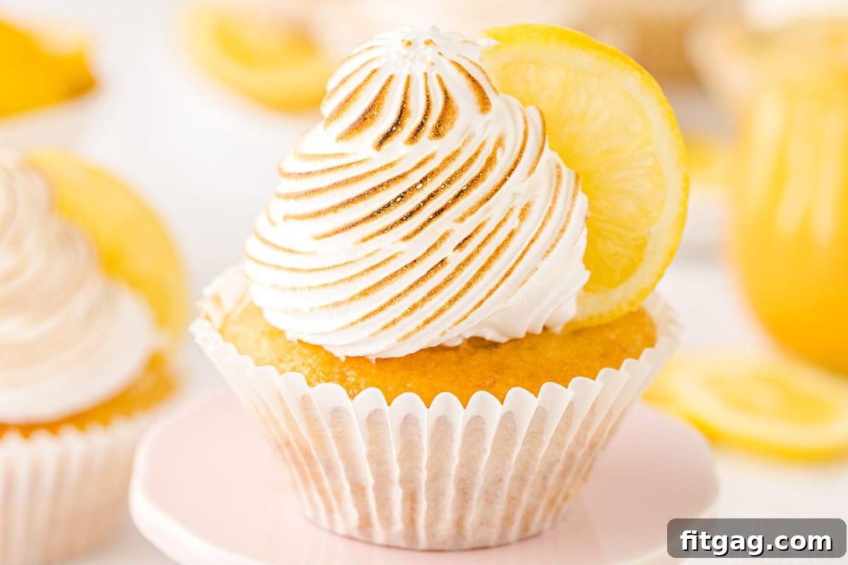 Tangy Meringue Cloud Cupcakes 6 A single perfectly crafted lemon meringue cupcake on a pastel pink cupcake stand, with a jar of lemon curd visible in the background, showcasing its delicate texture and filling.