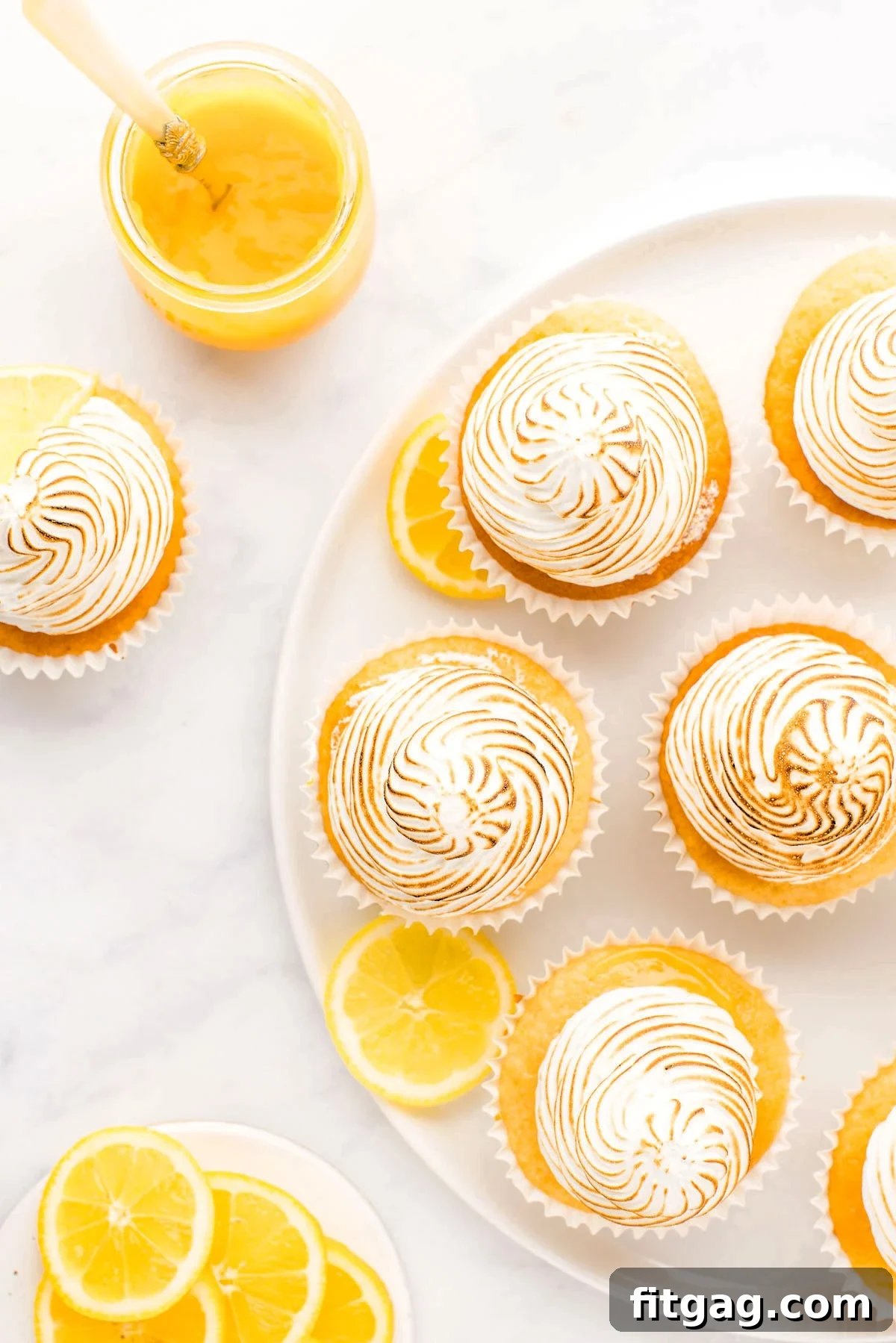 Tangy Meringue Cloud Cupcakes 7 A white plate showcasing six perfectly arranged lemon meringue cupcakes, accompanied by a bowl of fresh lemon wedges, highlighting their vibrant appeal.