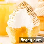 lemon meringue cupcake with bite taken showing the lemon curd in the middle of the cupcake and the pretty white interior of the meringue.