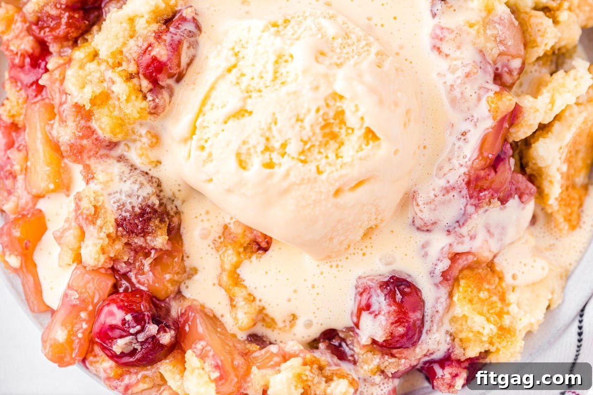 A top-down close-up view of a generous serving of cherry pineapple dump cake, topped with a large scoop of vanilla ice cream, just beginning to melt into the warm cake.