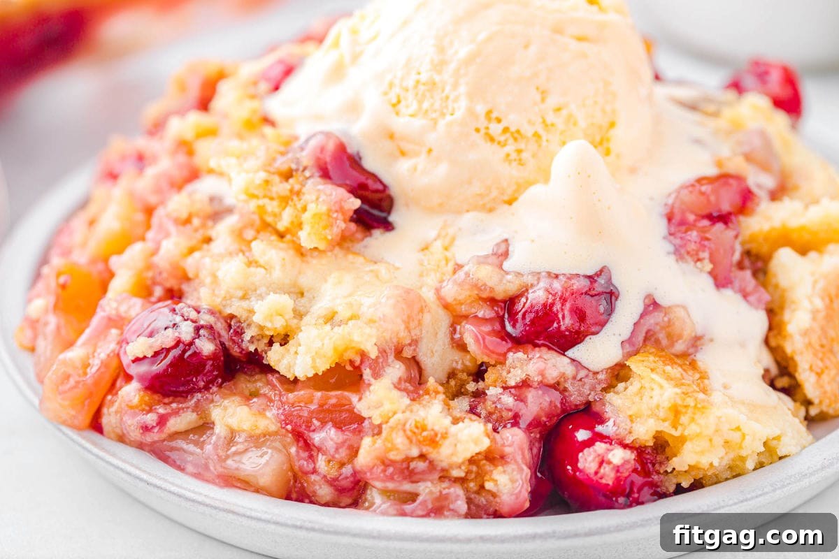 A shallow plate generously filled with a serving of pineapple cherry dump cake, topped with a scoop of vanilla ice cream that is gently melting into the cake.