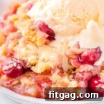 plate filled with cherry pineapple dump cake and topped with a scoop of vanilla ice cream that is just beginning to melt. cherries and pineapple chunks are visible in the cake.
