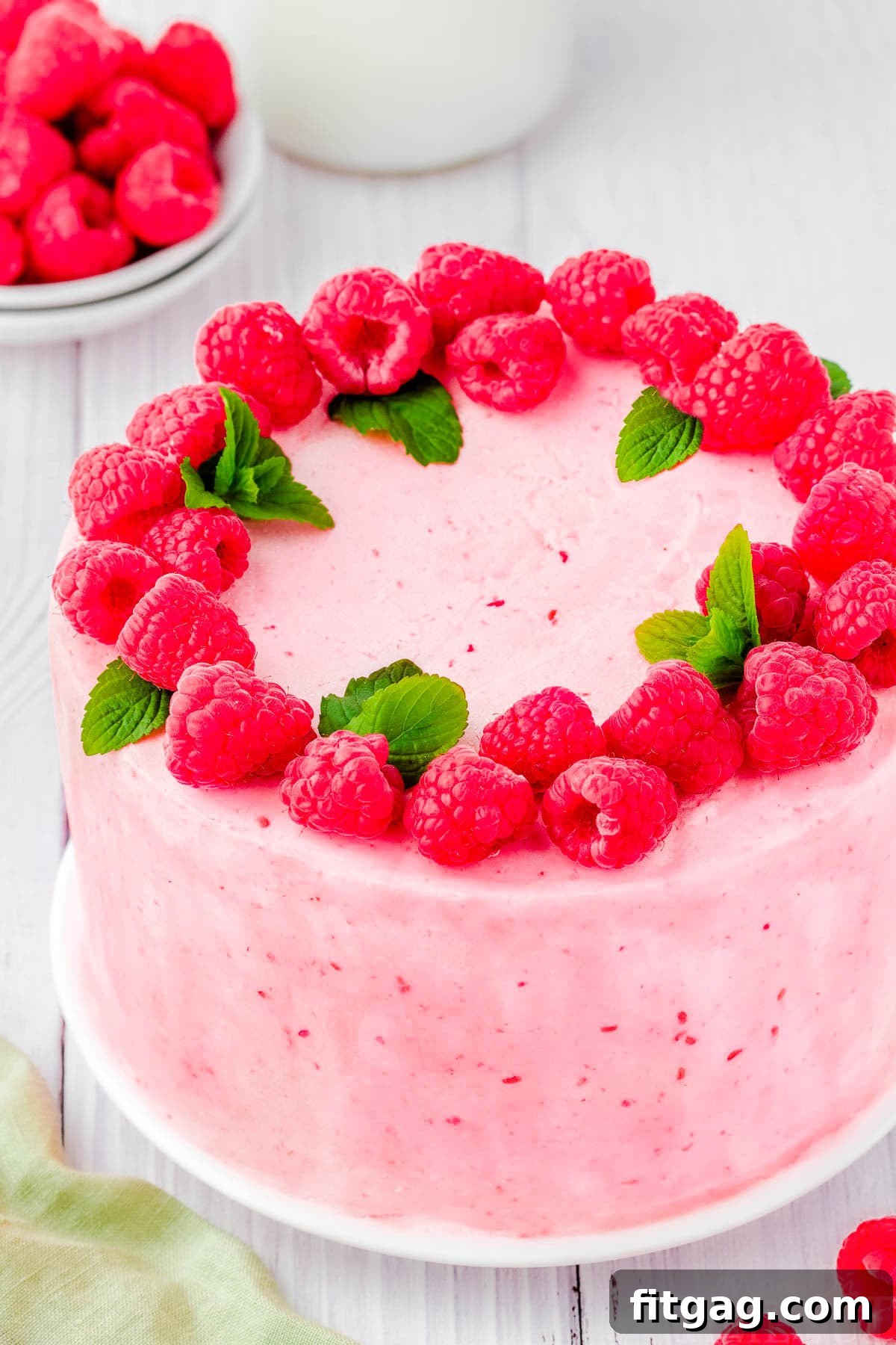 Luscious Raspberry Vanilla Cake 3 A full, uncut vanilla cake featuring beautiful raspberry buttercream and a generous raspberry filling. The cake is lavishly topped with dozens of fresh, ripe raspberries and sprigs of fragrant mint, ready to be served.