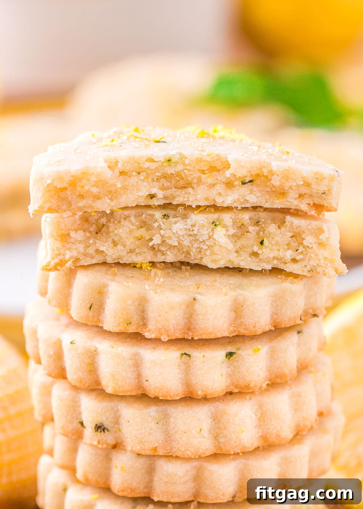 Zesty Lemon Basil Shortbread 3 A tall stack of approximately ten lemon shortbread cookies, with the topmost cookie elegantly broken in half to reveal its delicate, buttery crumb. The golden edges suggest a perfect bake.