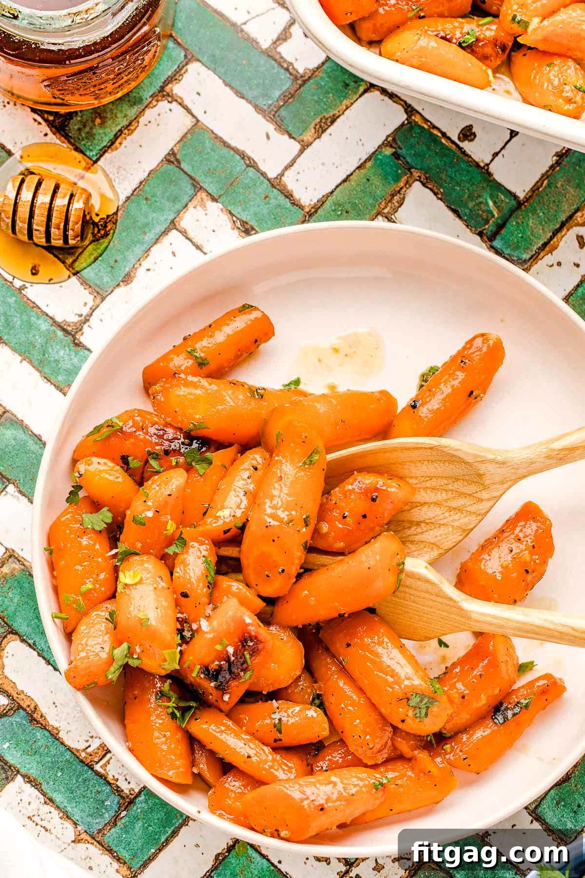 Honey Kissed Carrots 2 Honey glazed carrots on a round white plate, garnished with fresh parsley. The plate rests on a teal and white chevron tile surface.