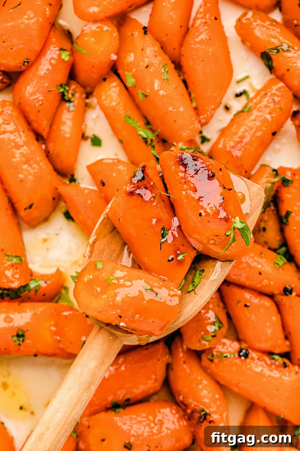 Honey Kissed Carrots 3 Honey glazed carrots on a baking sheet, featuring a wood spoon holding up three carrots, all made with honey and garlic.