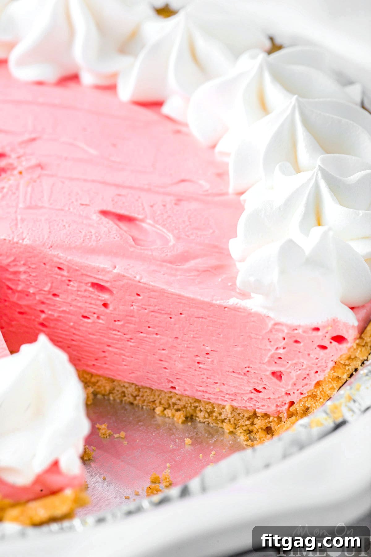 A vibrant strawberry Kool Aid pie, perfectly set within a golden graham cracker crust, with one enticing slice already removed, showcasing its smooth, creamy interior.