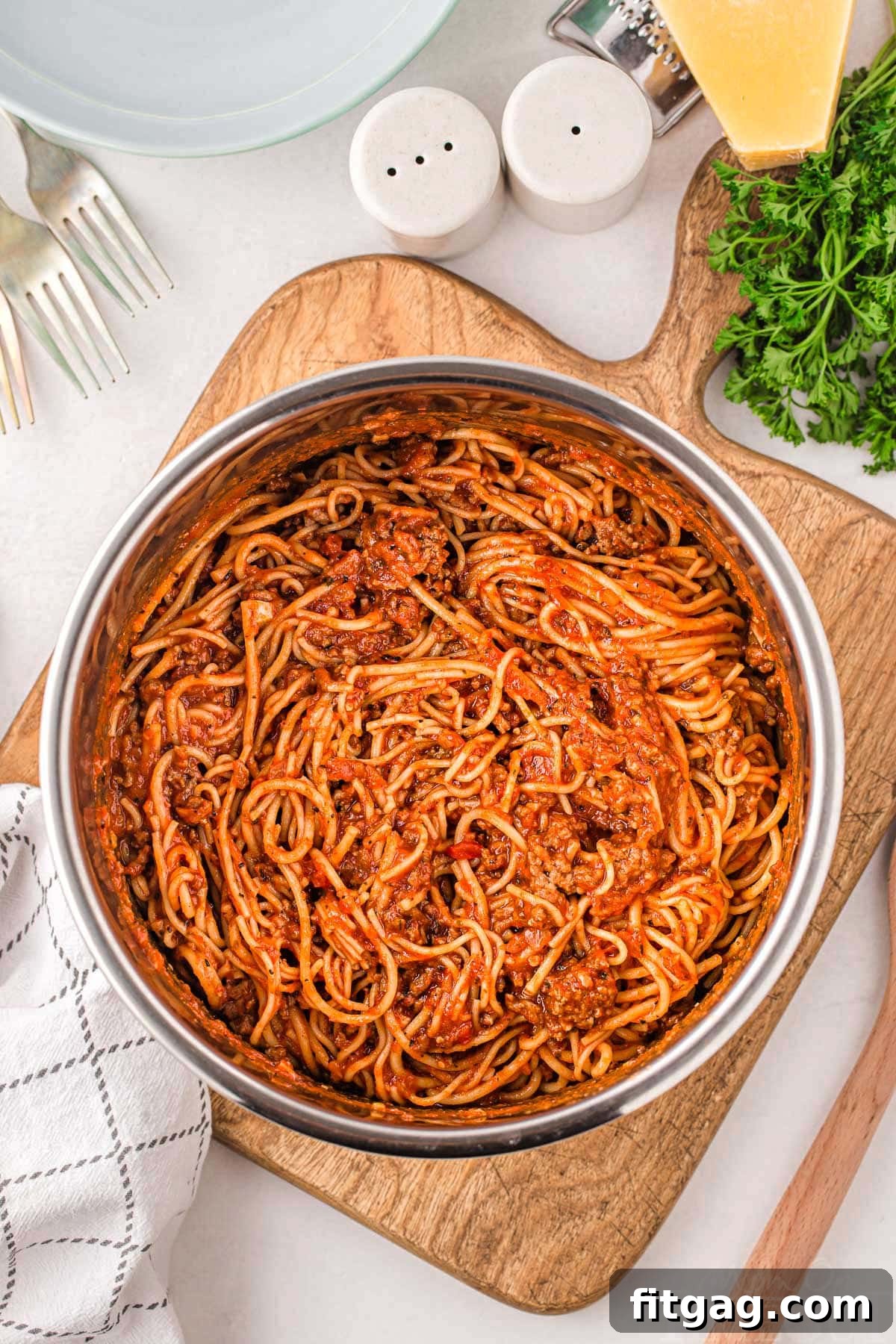 One Pot Instant Pot Spaghetti 2 A vibrant serving of Instant Pot Spaghetti, garnished with fresh parsley and grated Parmesan cheese, sits on a rustic wooden cutting board, ready to be enjoyed. The rich meat sauce and perfectly cooked noodles promise a delightful meal.