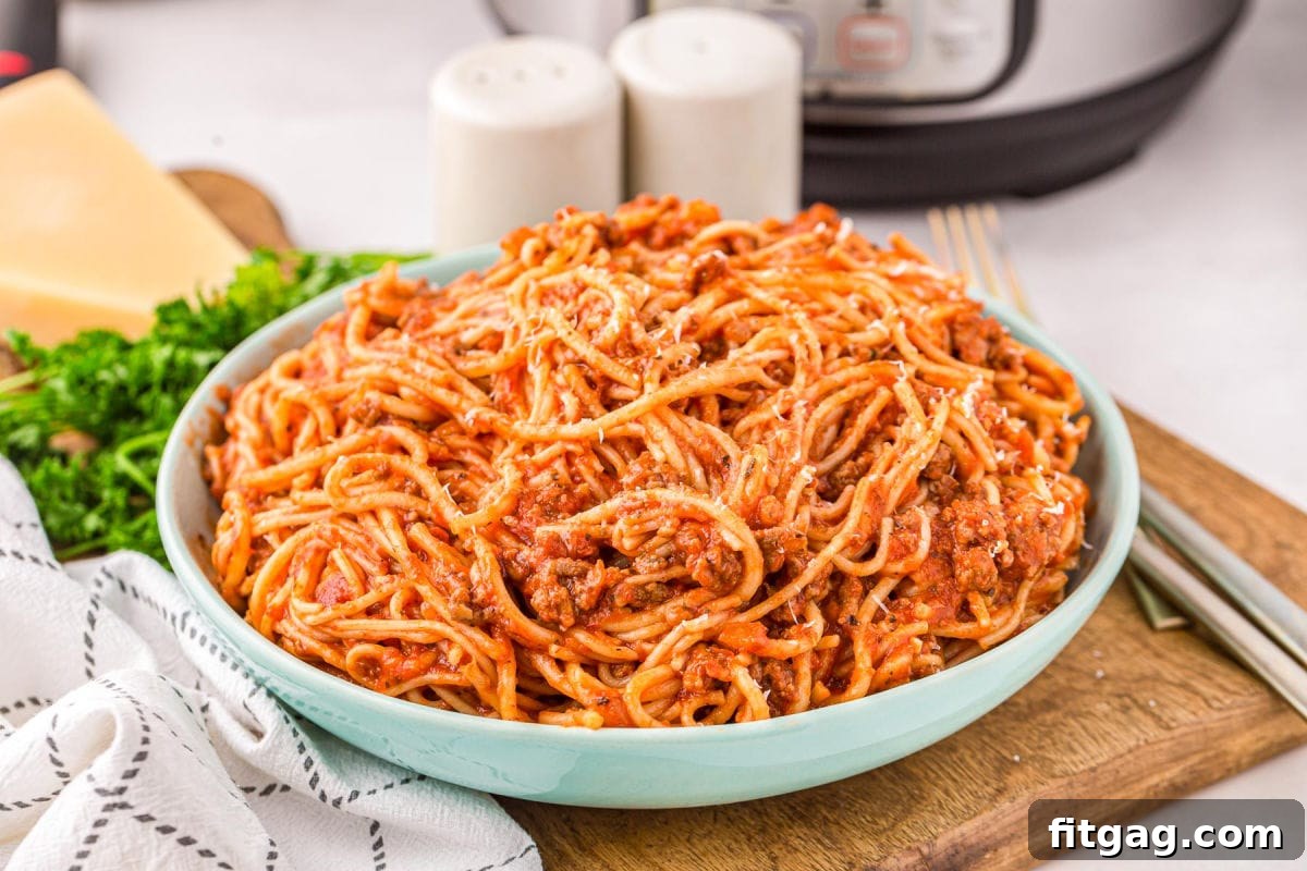 One Pot Instant Pot Spaghetti 4 A charming aqua blue serving bowl, generously filled with steaming Instant Pot Spaghetti, rests on a wooden board next to a white linen towel, with the pressure cooker subtly visible in the background, hinting at its quick preparation.