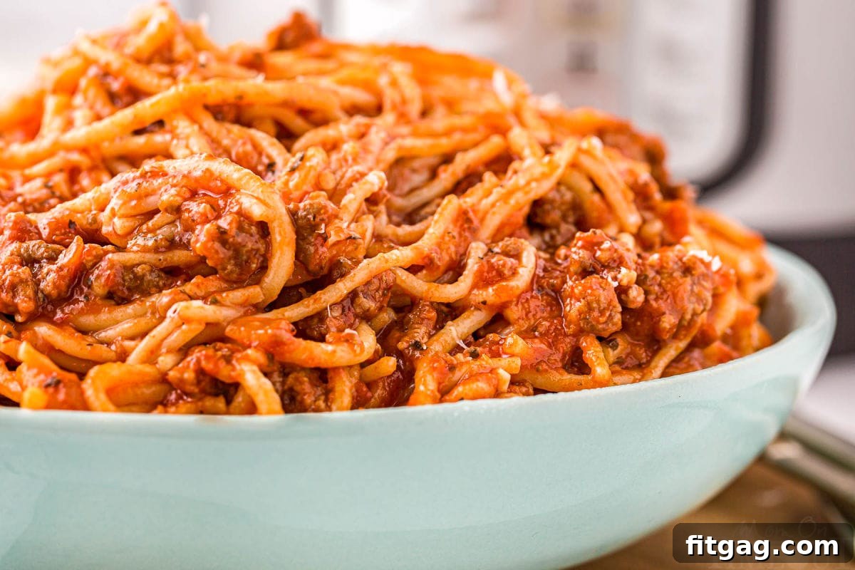 One Pot Instant Pot Spaghetti 6 A close-up shot of a large aqua serving bowl brimming with savory Instant Pot Spaghetti, topped with a generous sprinkle of freshly grated Parmesan cheese and vibrant fresh basil leaves, ready to be devoured.