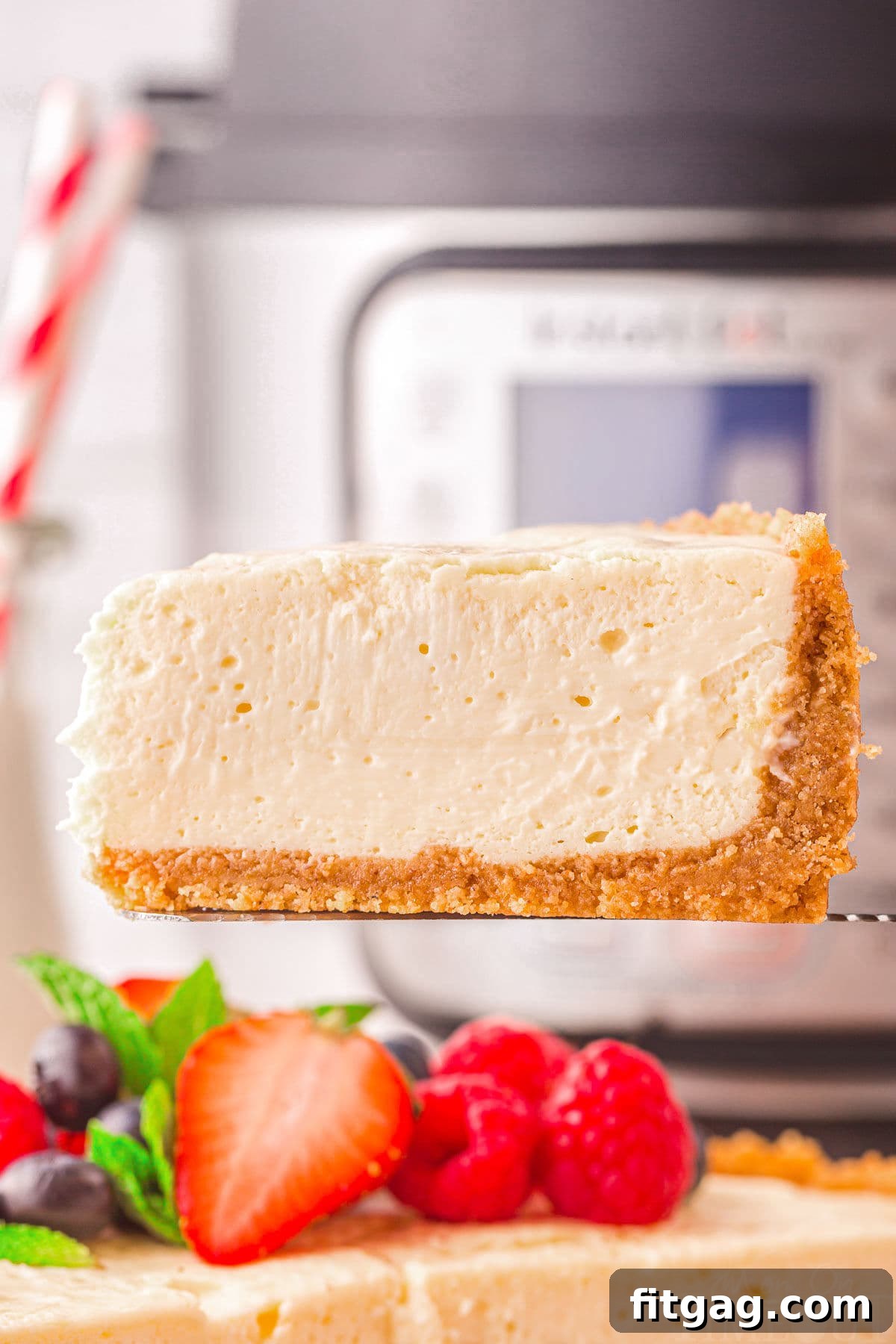 one slice of instant pot cheesecake being held above the rest of the cheesecake in front of an instant pot.