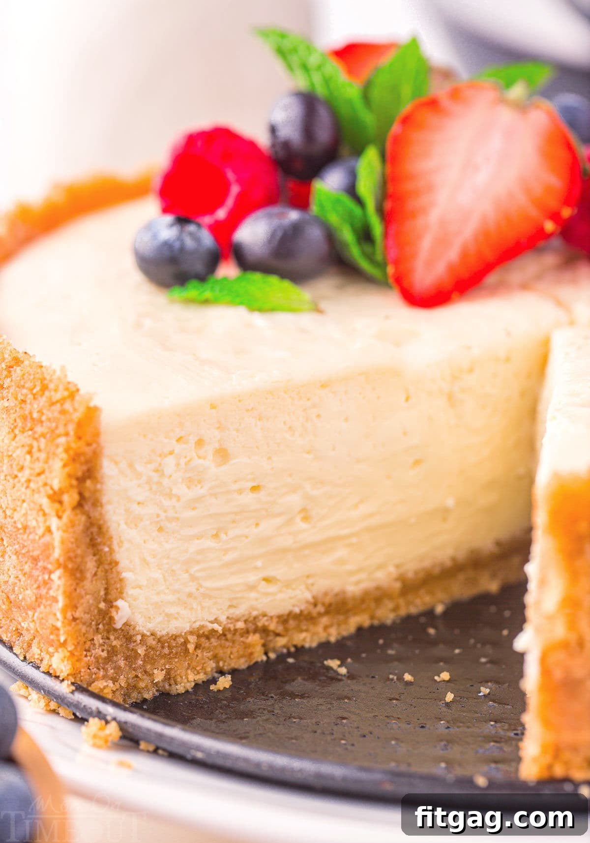 close up look at interior of cheesecake with one slice removed. fresh berries and mint can be seen on top of the cheesecake.