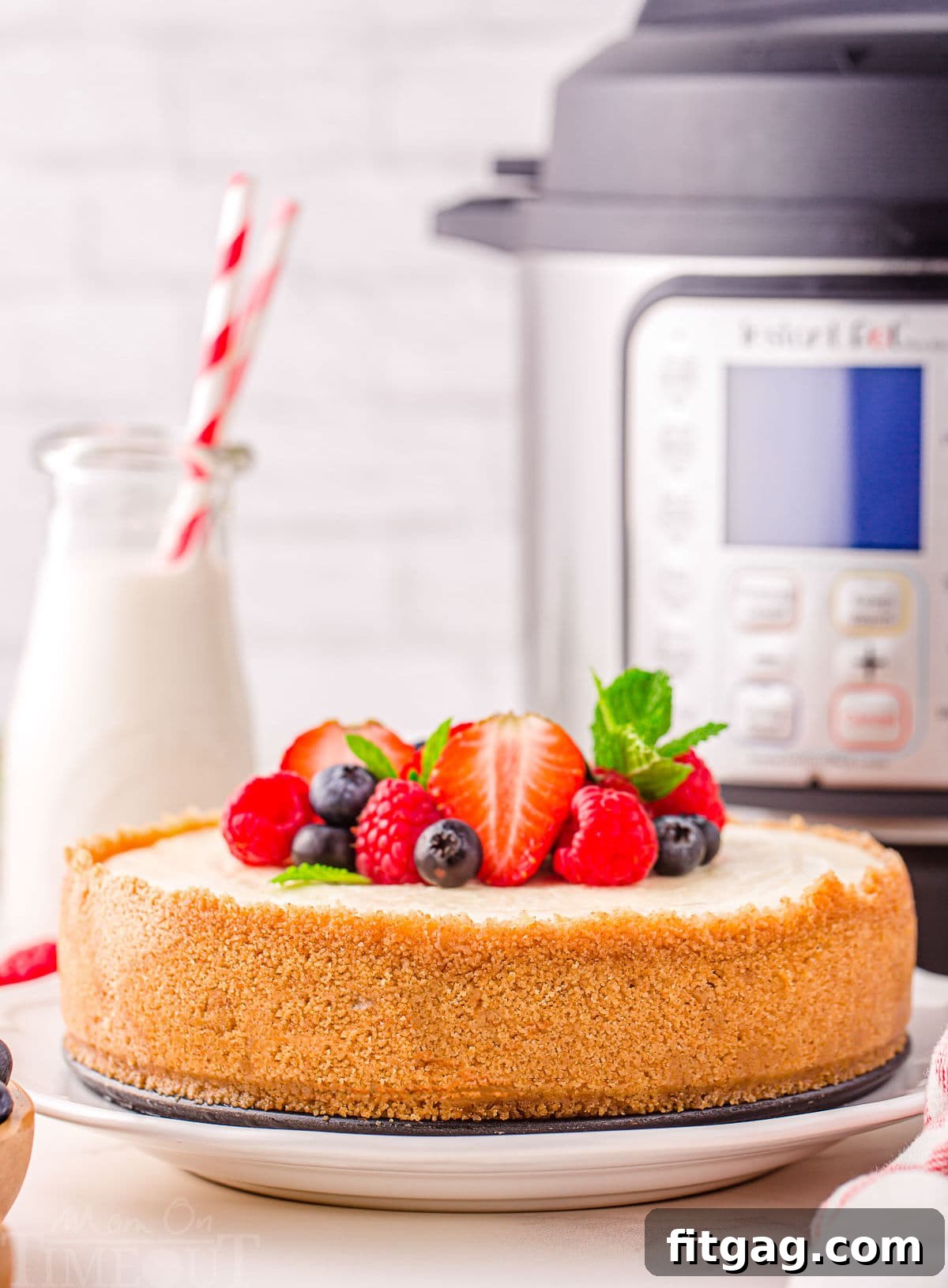 whole cheesecake sitting in front of instant pot with berries on top.