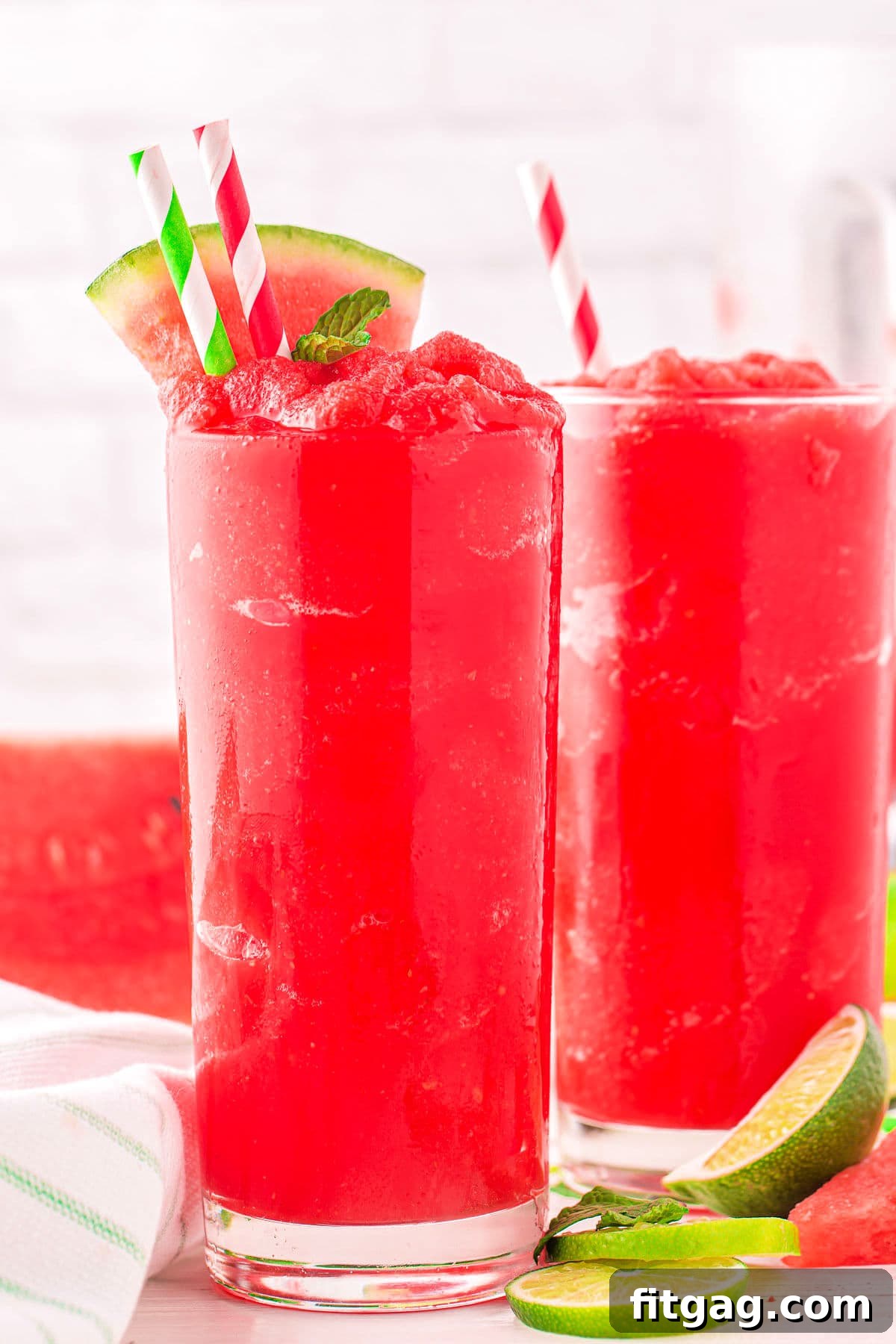 Two tall glasses brimming with bright red watermelon slushie, garnished with fresh watermelon wedges, ready to be enjoyed.