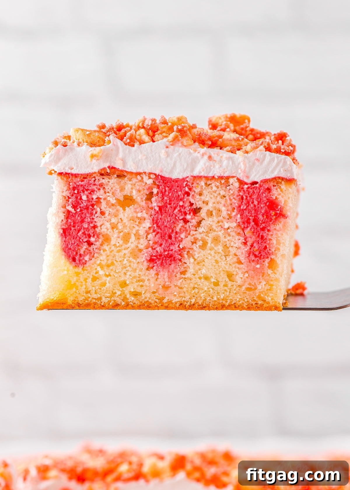slice of strawberry poke cake recipe held up above the rest of the cake.