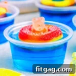 blue pool party jello shot with gummi bear sitting on white surface. more jello shots can be seen in the background.