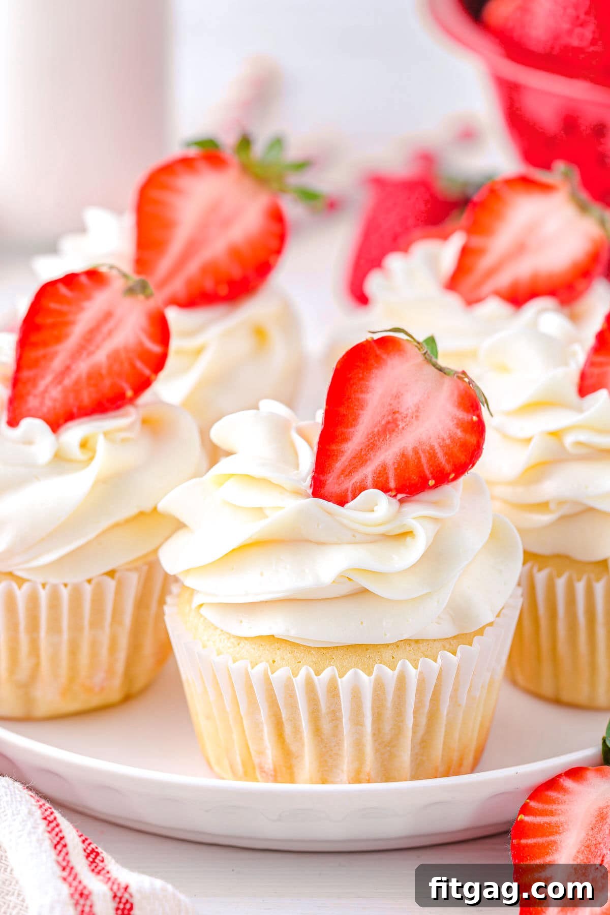 Five strawberry shortcake cupcakes beautifully arranged on a white plate, each topped with a strawberry half and a generous swirl of buttercream frosting.