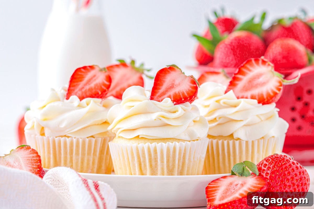 Five vanilla cupcakes topped with vanilla buttercream and filled with strawberry jam, presented on a white plate, ready to be enjoyed.