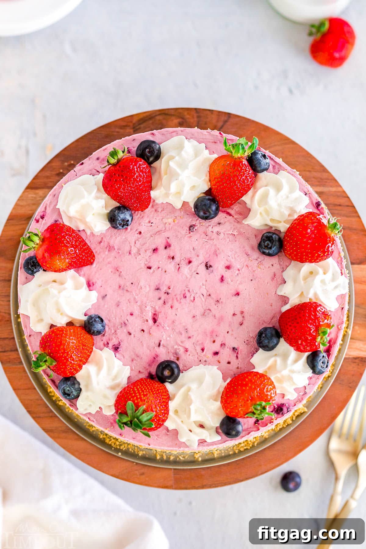 A stunning top-down view of a No Bake Berry Cheesecake, beautifully decorated with an assortment of fresh berries and elegant dollops of whipped cream, ready to be served.