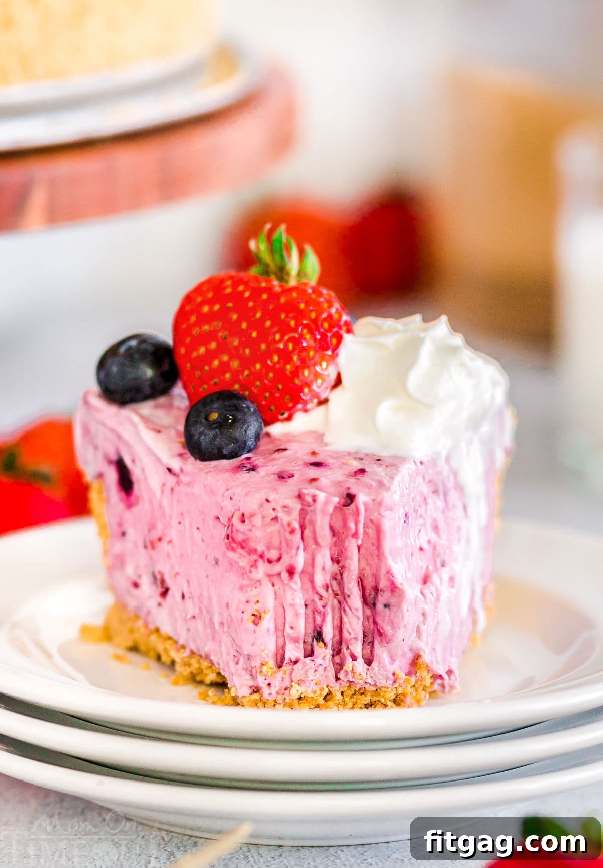 A pristine slice of No Bake Berry Cheesecake resting on a small, round white plate, with a fork removing a perfect bite from its tip, highlighting its creamy texture.