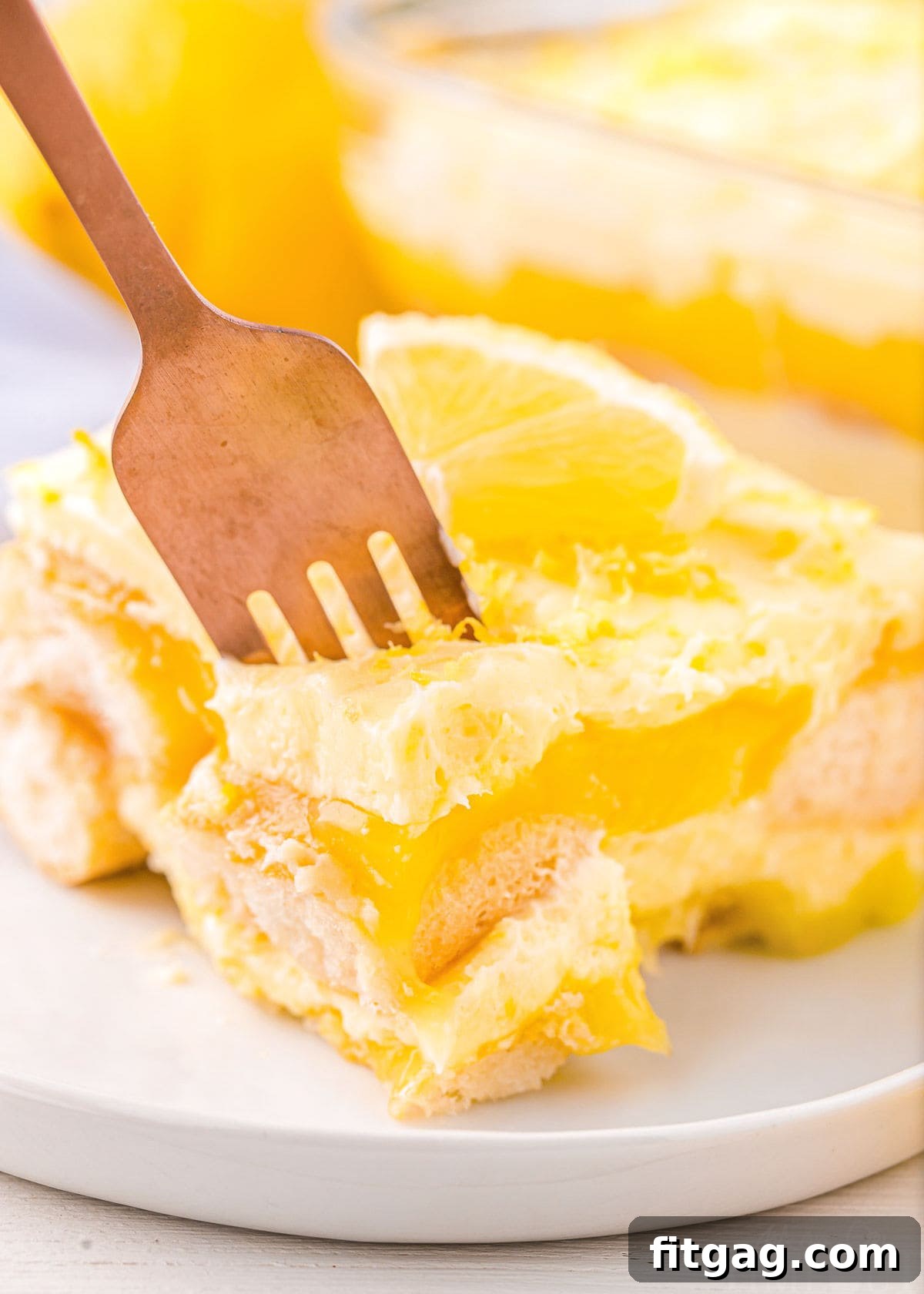 A fork lifting a delicious bite of Lemon Tiramisu from a round white plate, highlighting the creamy texture.
