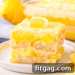 layered lemon tiramisu dessert cut into a square on a white dessert plate with the rest of the dessert in the background.
