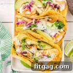 top down view of four fish tacos on a white rectangle plate with avocados and cilantro and lime wedges around the plate.