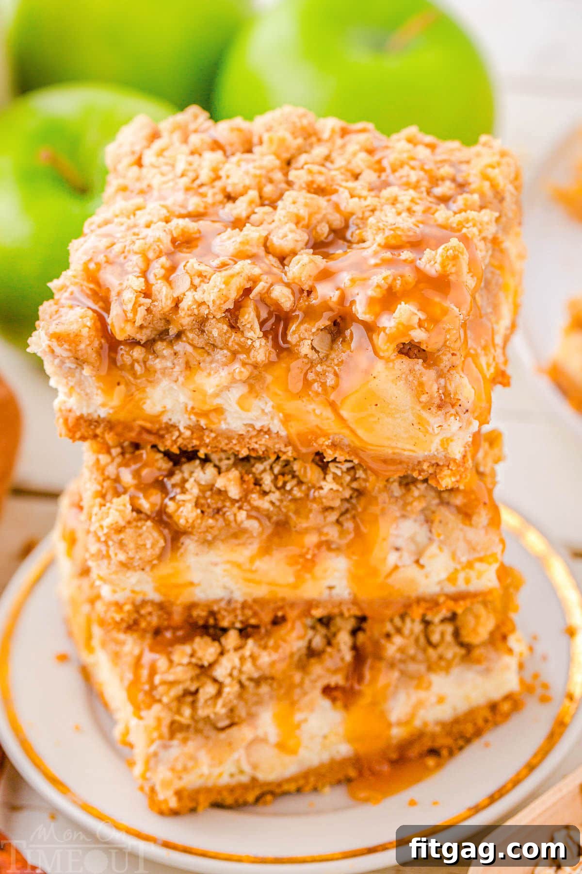 Three caramel apple cheesecake bars stacked neatly on a white plate. Each bar features distinct layers and a rich caramel drizzle, highlighting the inviting crumb topping.