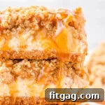 Two caramel apple cheesecake bars stacked on a white plate with a gold rim, caramel sauce is drizzled on top of the bars.
