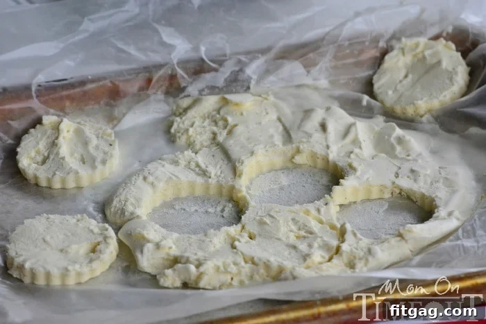 Ice cream circles cut with a cookie cutter on a baking sheet, ready for sandwich assembly.
