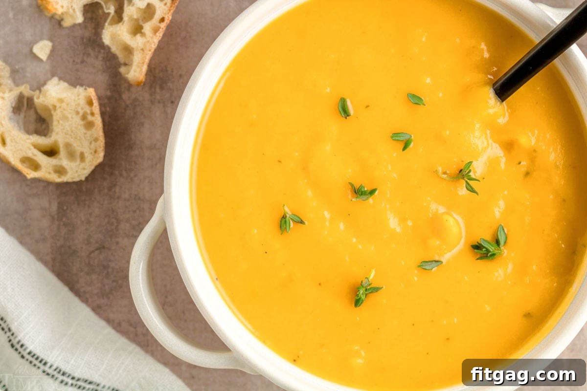 A top-down shot of vibrant orange roasted butternut squash soup in a pristine bright white round bowl, beautifully garnished with fresh thyme leaves for a touch of freshness.