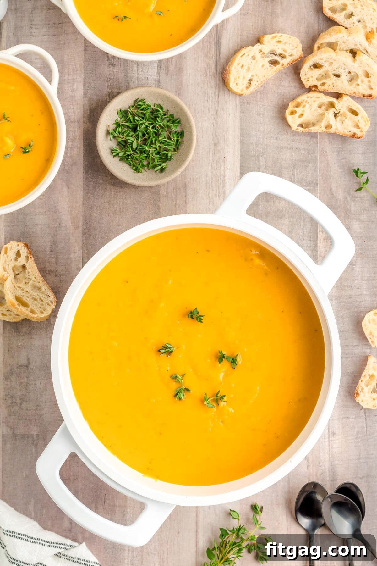 A top-down perspective of vibrant orange butternut squash soup served in a large white bowl, flanked by two smaller white bowls containing various delicious toppings for customization.
