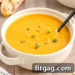 White round bowl filled with butternut squash soup topped with fresh thyme. A black spoon is in the bowl.