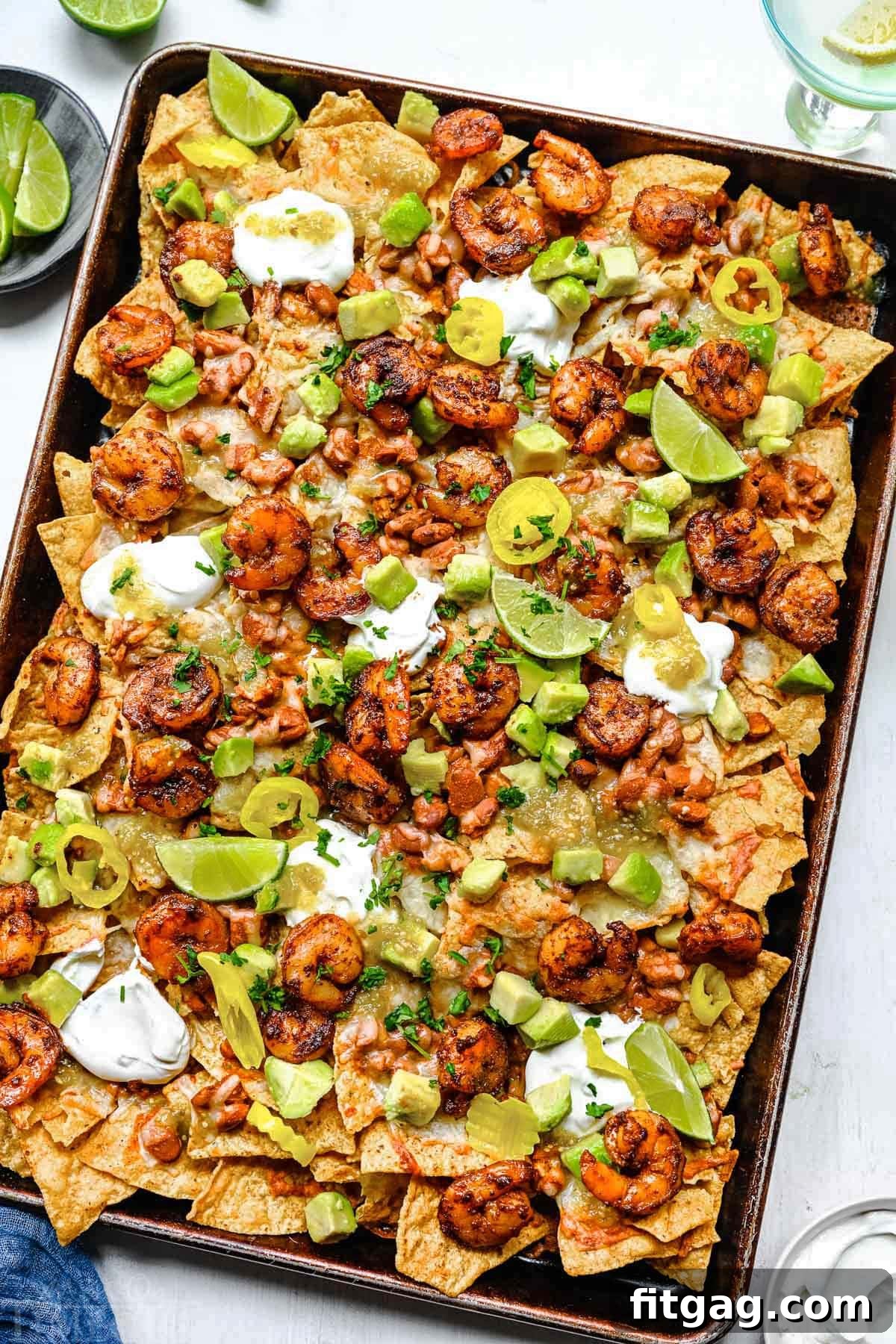 Fiesta Shrimp Crunch 3 A beautifully arranged top-down view of shrimp nachos presented on a sheet pan, artfully garnished with generous dollops of sour cream, slices of creamy avocado, and vibrant salsa.