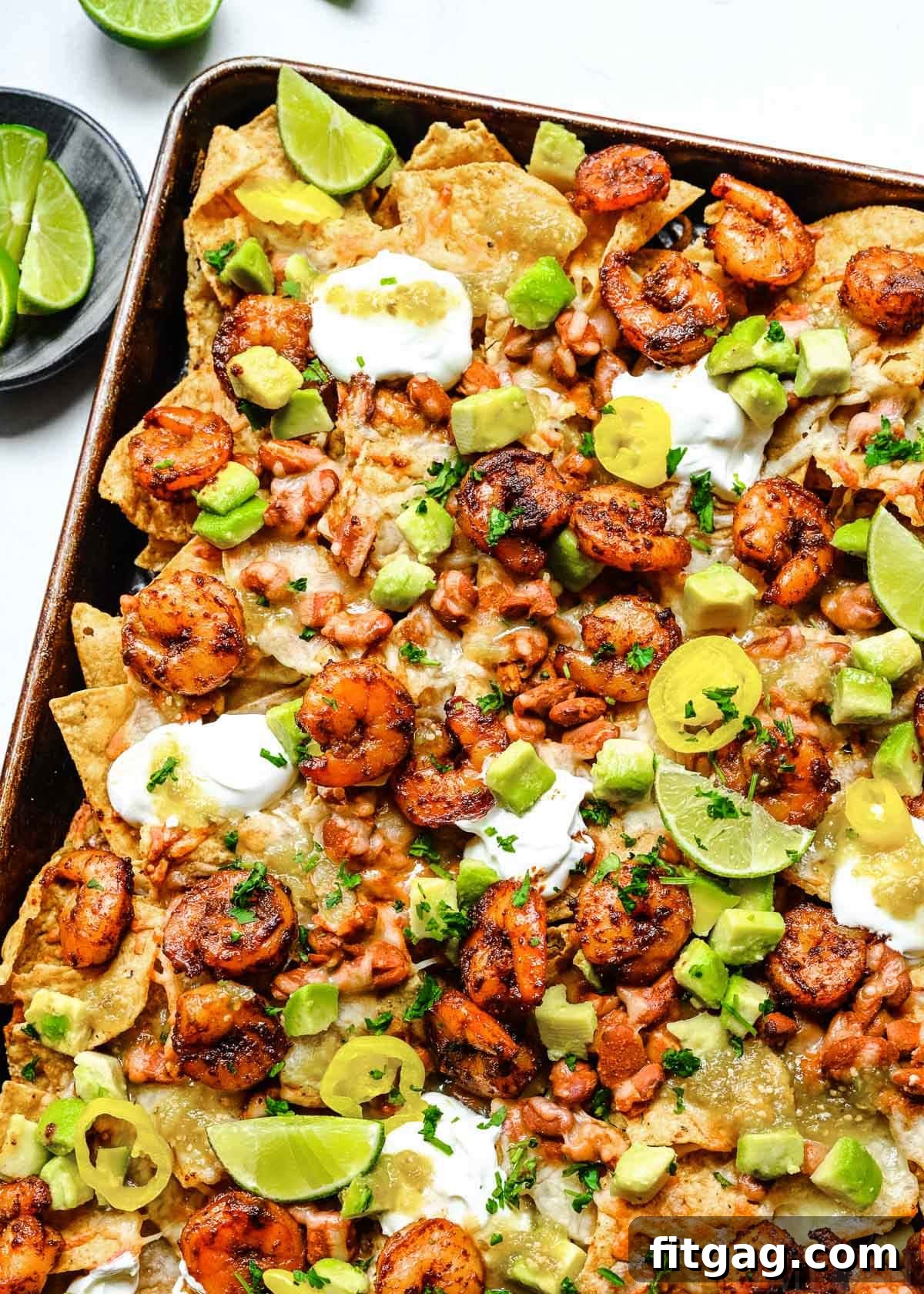 Fiesta Shrimp Crunch 5 A top-down view of a generously portioned sheet pan of shrimp nachos, brimming with colorful toppings including a dollop of sour cream, slices of fresh avocado, and vibrant salsa, ready to be enjoyed.