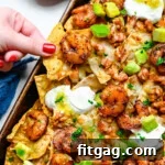 Fiesta Shrimp Crunch 6 shrimp nachos on a sheet tray with lots of topping. hand pulling a loaded chip off of the nachos.