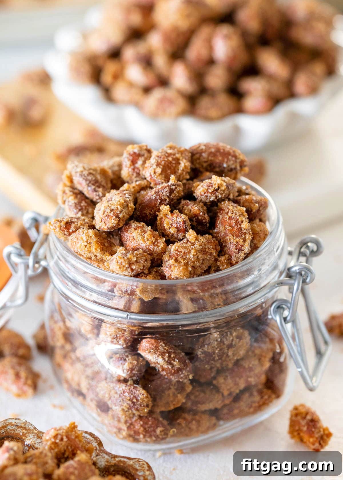 Glazed Almond Delights 2 candied almonds in a glass jar filled to overflowing. a small white bowl of candied almonds can be seen in the background.