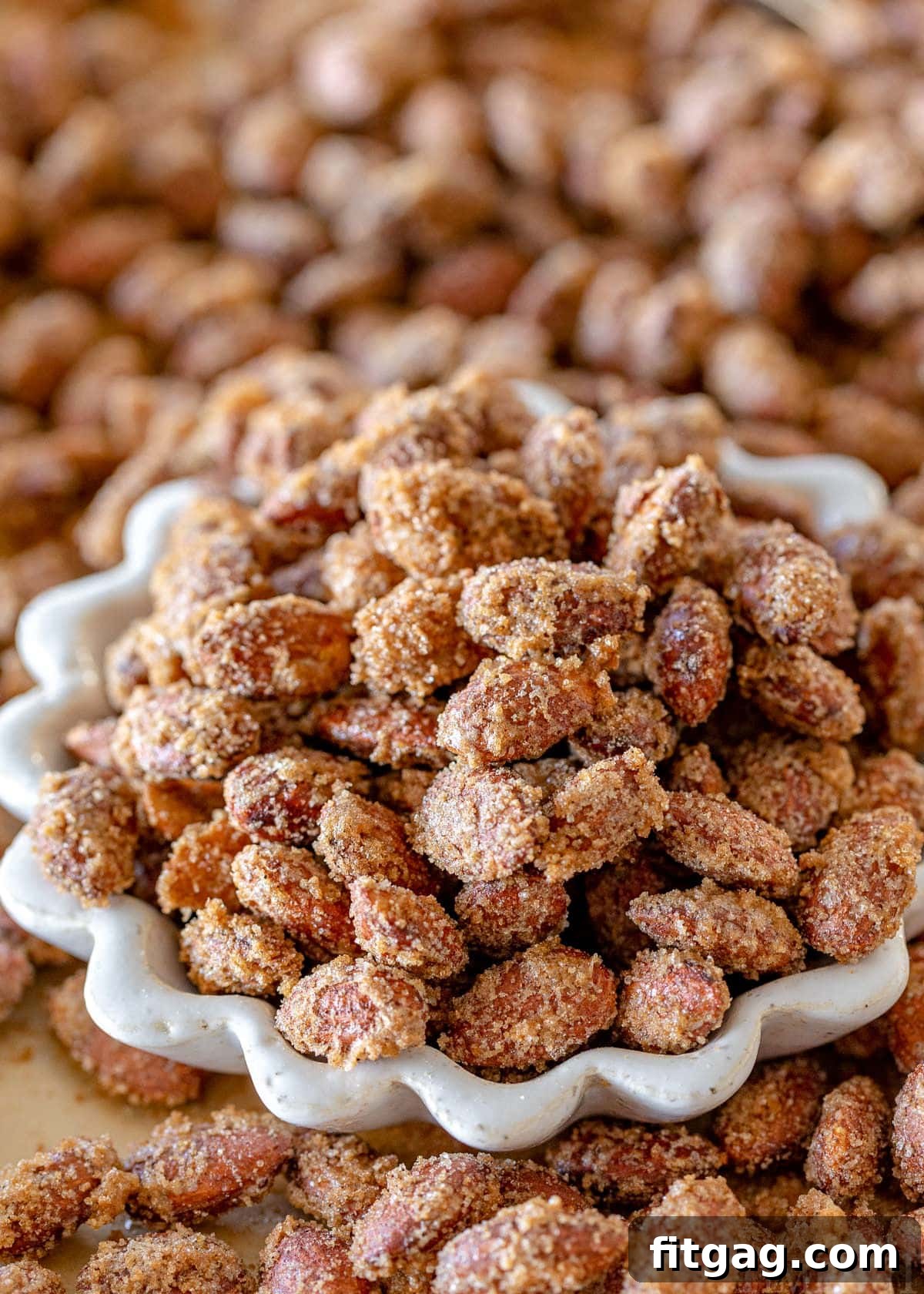 Glazed Almond Delights 5 homemade candied almonds recipe in a small white bowl surround with more almonds on a sheet pan.