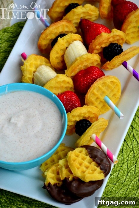 A hand dipping a fruit and waffle kabob into a bowl of maple cinnamon Greek yogurt dip, highlighting the creamy texture.