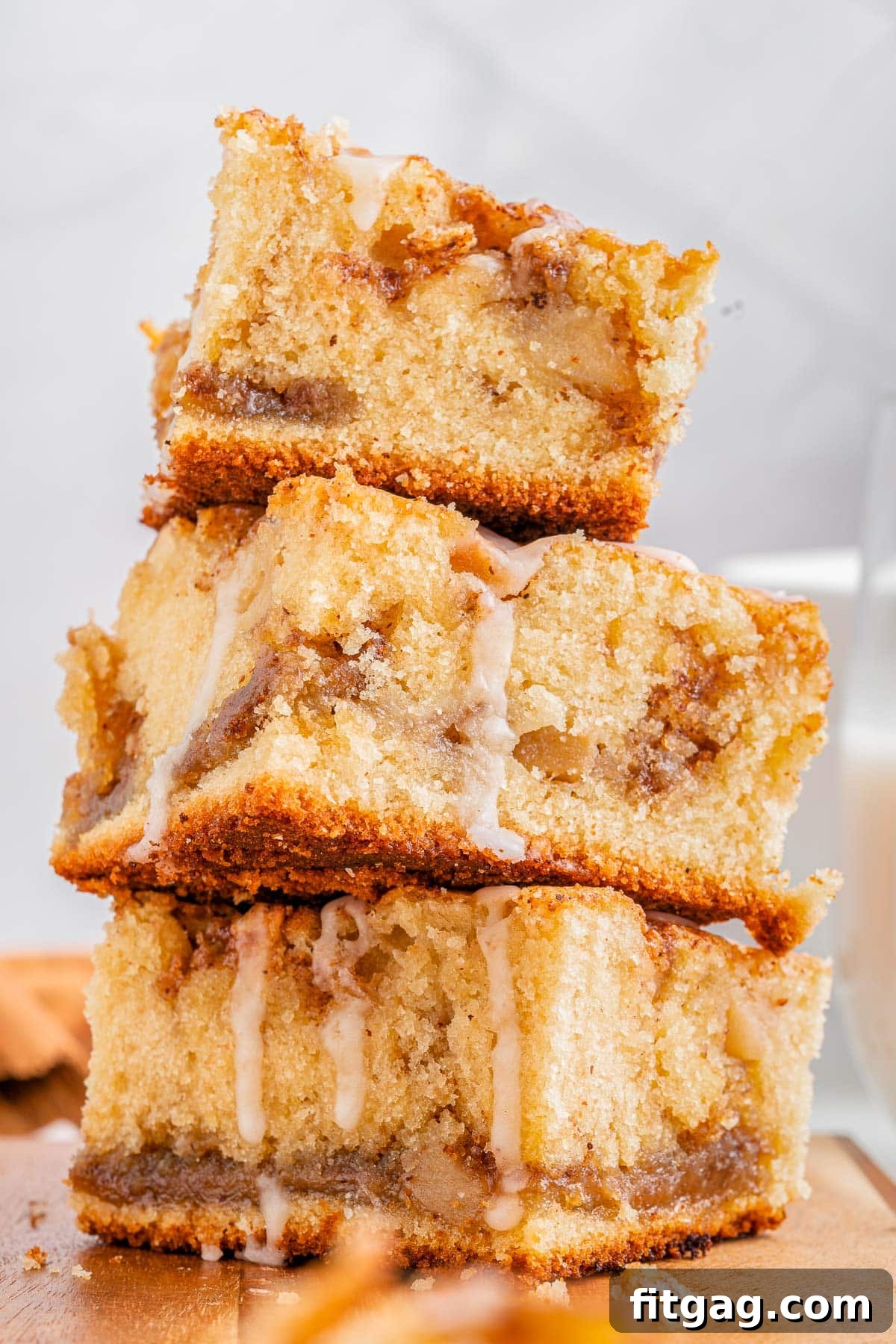 Autumn Apple Coffee Delight 3 three pieces of apple coffee cake stacked on a wood cutting board. glaze is drizzled down on top of the coffee cake pieces.
