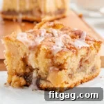 one piece of apple coffee cake sitting in front of a cutting board with three more pieces stacked together. coffee cake has a little glaze drizzled over the top.