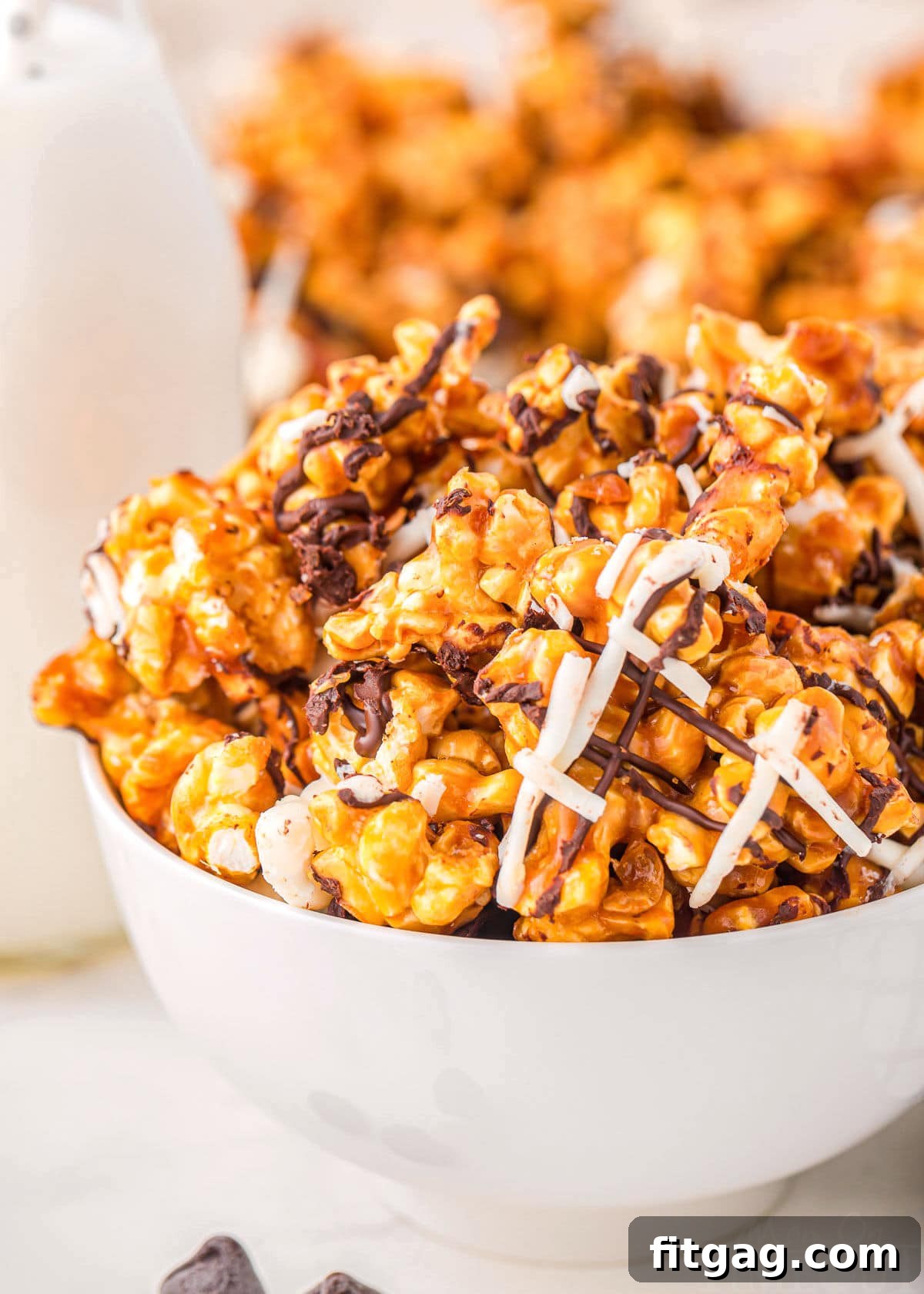 A crisp white bowl overflowing with beautifully striped Zebra Popcorn, showcasing the rich caramel and dual chocolate drizzles. A jar of milk is softly blurred in the background, hinting at a cozy snack time.