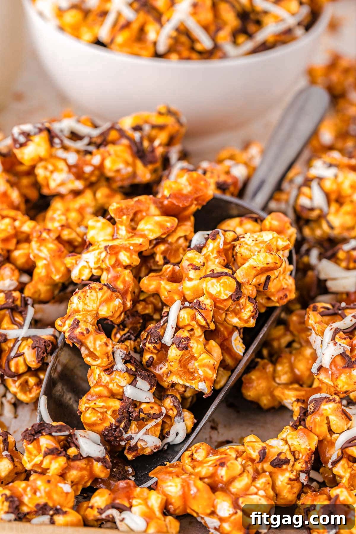 Zebra Swirl Popcorn 3 A large metal scoop gracefully lifts a generous portion of golden-brown caramel corn from a baking sheet, with a pristine white bowl waiting in the softly blurred background.