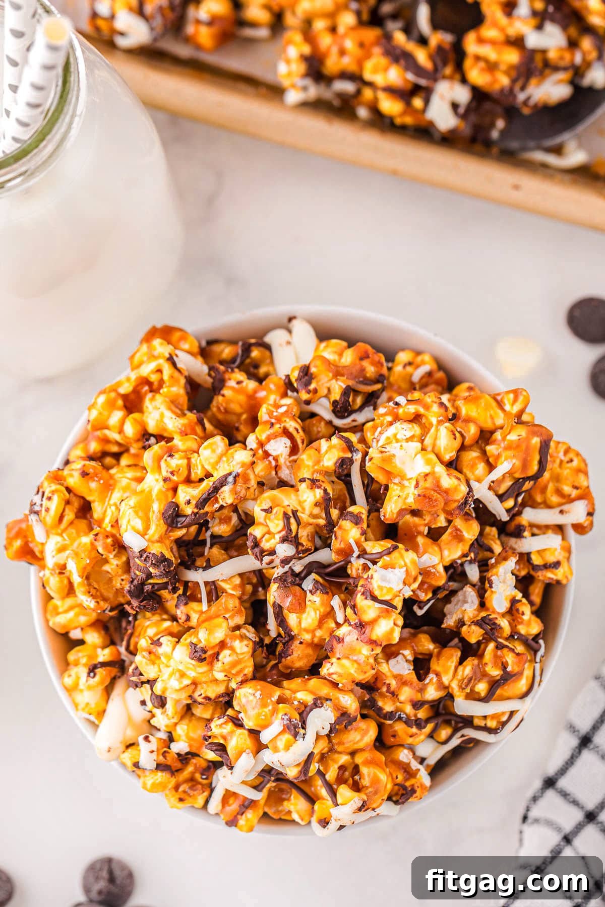 Zebra Swirl Popcorn 5 A captivating top-down view of caramel corn artfully arranged in a pristine white bowl on a smooth marble surface. The popcorn is elegantly drizzled with contrasting stripes of white and dark chocolate, showcasing the iconic 'zebra' pattern.