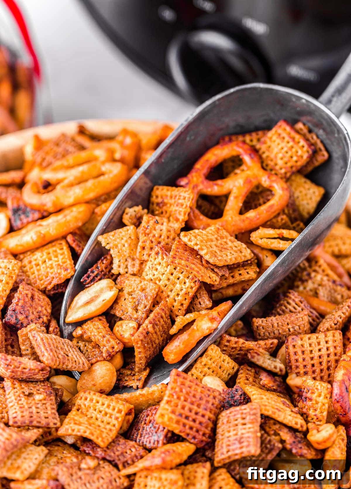 Slow Cooker Chex Mix Perfection 3 A large wooden bowl brimming with freshly made slow cooker Chex Mix, with a metal scooper poised to serve. A black slow cooker is visible in the background, hinting at the ease of preparation.