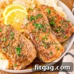 Three perfectly seared honey garlic pork chops resting on a bed of creamy mashed potatoes, garnished with fresh parsley and vibrant lemon slices. The plate is beautifully presented on a rustic wooden board.