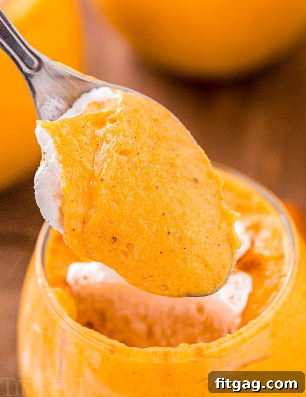 Creamy Pumpkin Cloud 3 one spoonful of pumpkin mousse taken out of glass topped with whipped cream and held up over the glass.