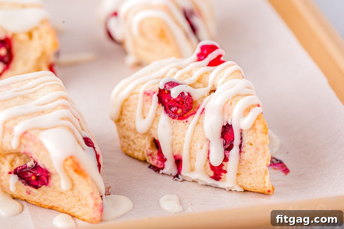 Tangy Cranberry Scones 4 four cranberry scones on a parchment lined baking sheet topped with a simple glaze.