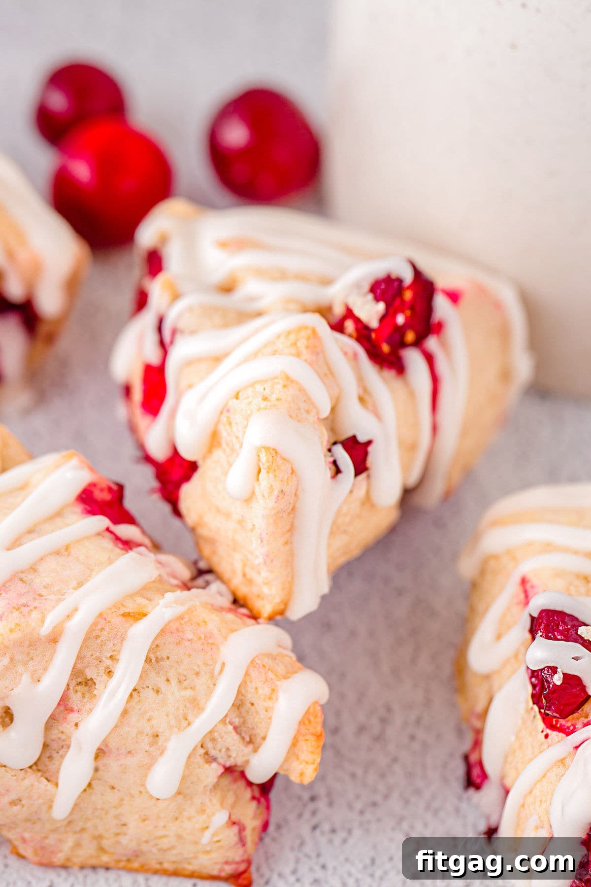 Tangy Cranberry Scones 5 easy cranberry scones with glaze sitting on white surface with fresh cranberries scattered about.